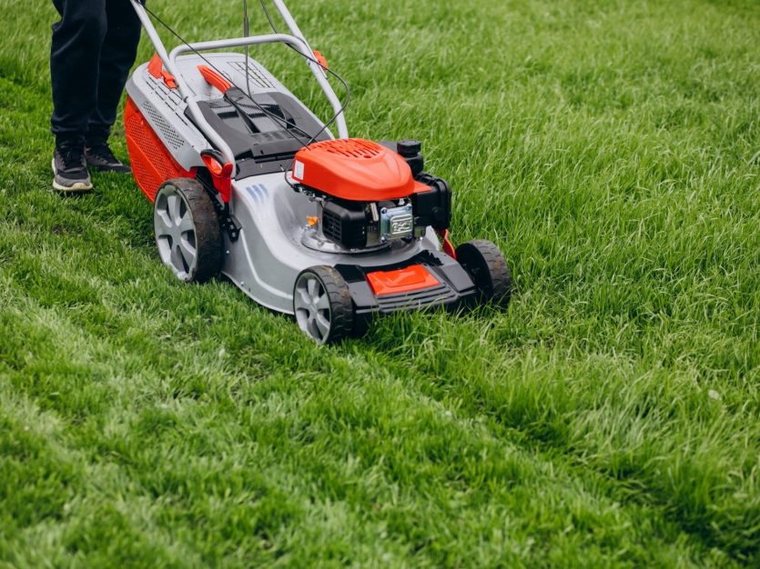 A person using the lawn mower to trim grass.