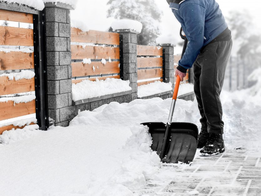 Man shoveling snow from street in winter with shovel after snowstorm.