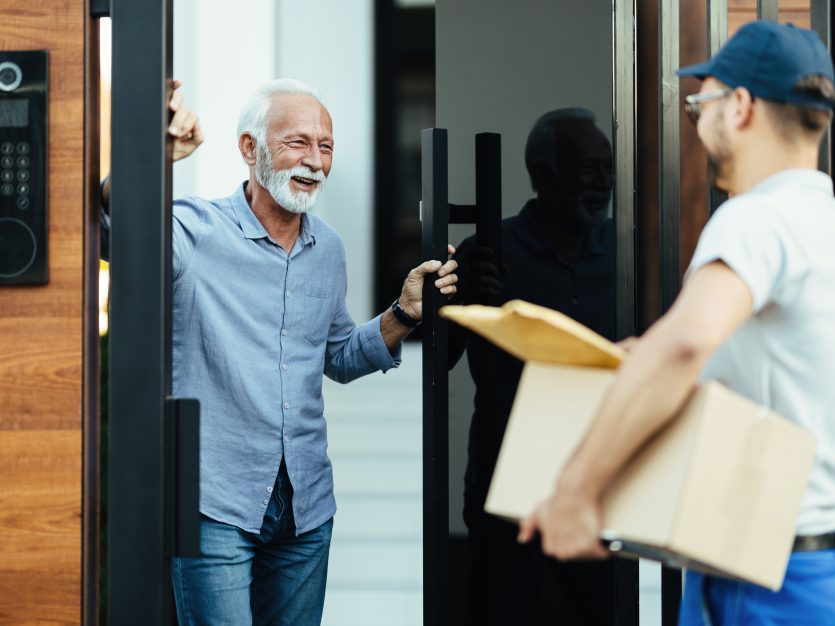 Happy mature man standing at the gate and talking with courier who is delivering medicines.