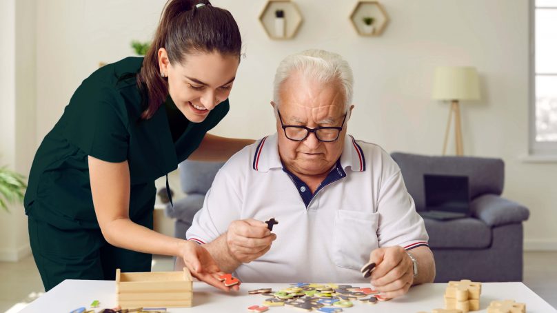 A woman guides an elderly man through a puzzle, highlighting their interaction and the joy of shared activities in their time together.