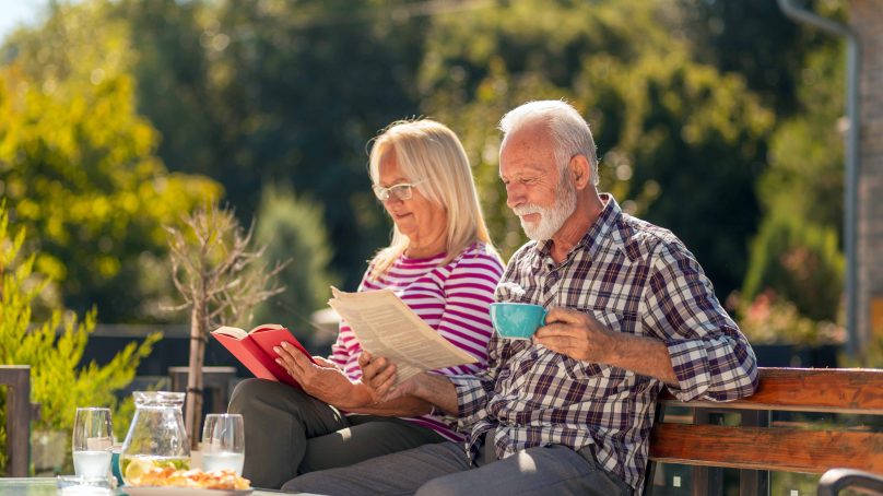 A senior couple enjoys reading a book together while sipping coffee in a serene garden setting.