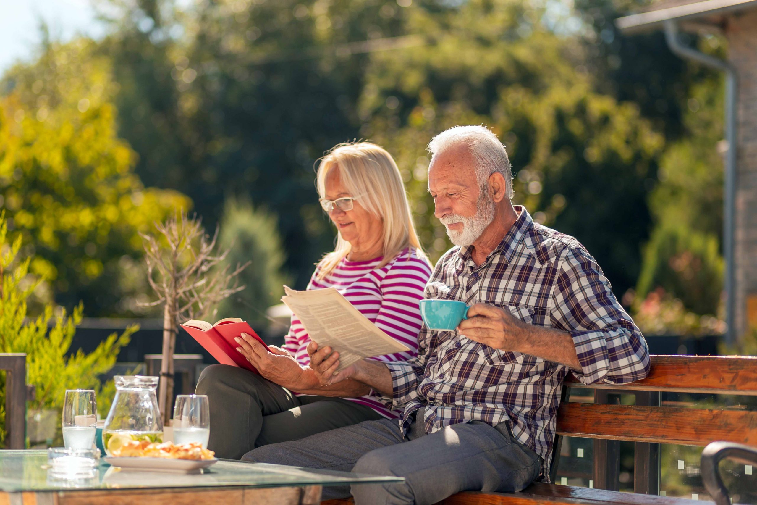 A senior couple enjoys reading a book together while sipping coffee in a serene garden setting.