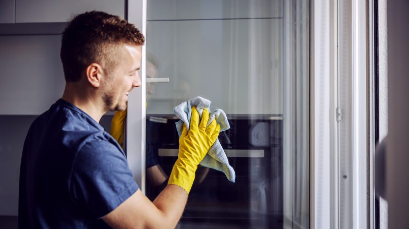 Young man with rubber gloves cleaning window with cloth.