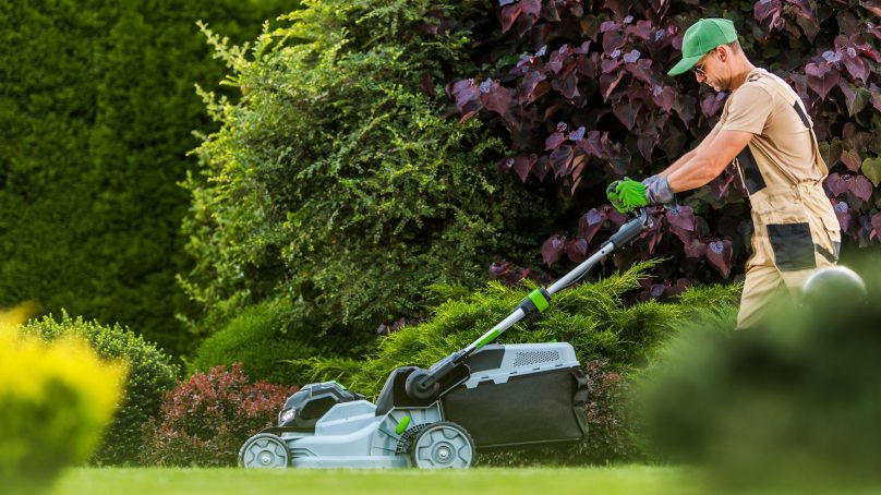 Garden Worker with lawn mower cutting residential grass