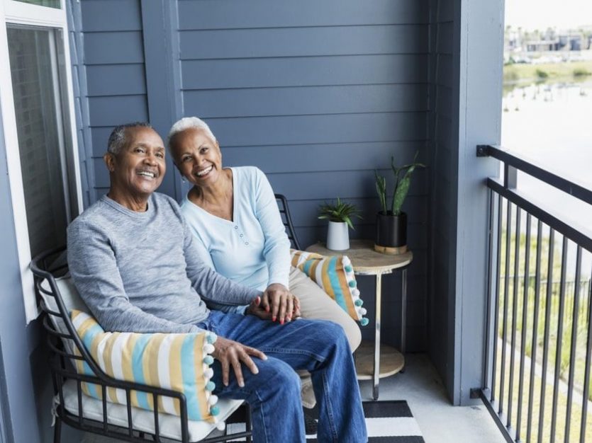 Home care - An elderly couple peacefully seated on a balcony, pondering the decision of aging in place versus moving to a retirement home.