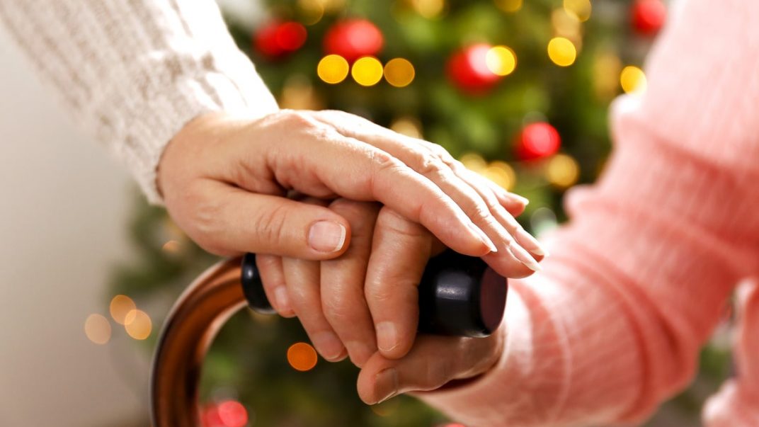 A caring woman supports an elderly person by holding their hand, showing compassion and companionship.