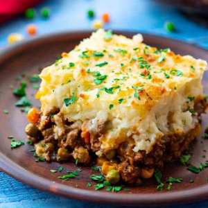 Beef shepherds pie topped with greens on a plate.