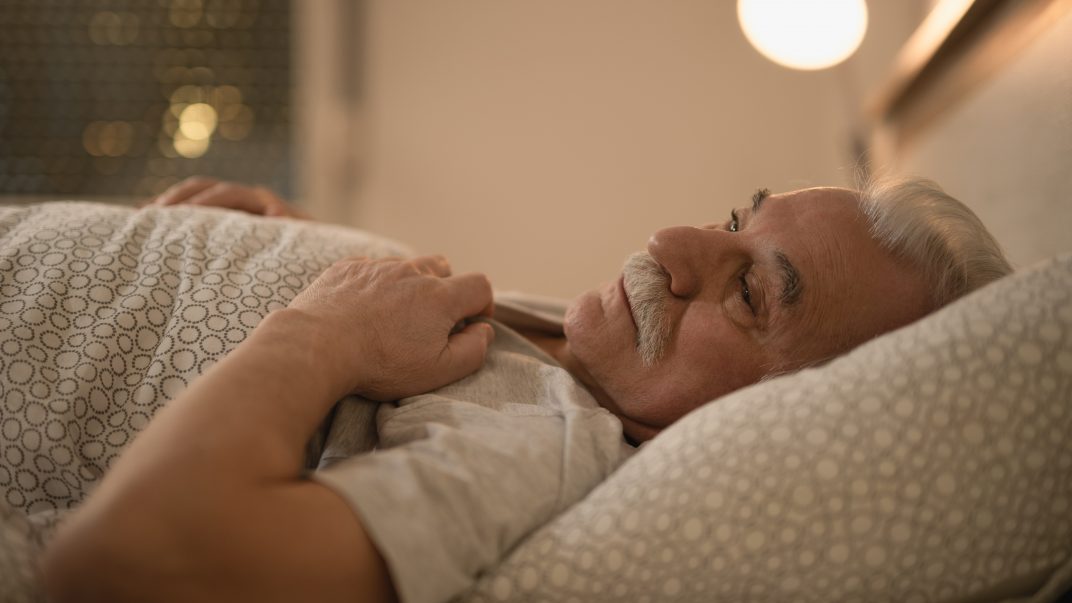 Sleep changes with age: Sleepless mature man thinking while lying down in bed in the evening.