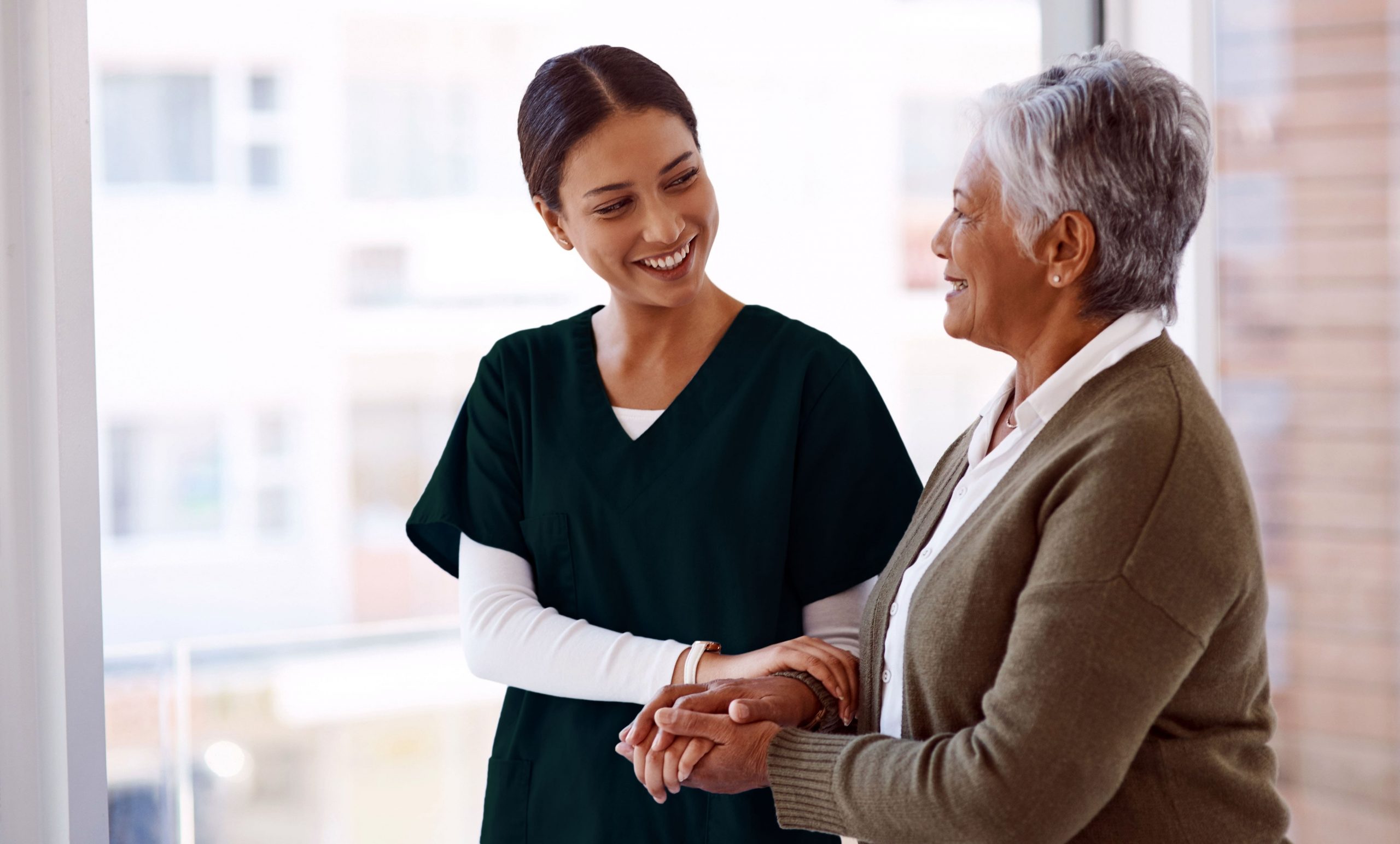 A nurse and an elderly woman smiling as they shake hands, symbolizing care and connection in a healthcare setting.