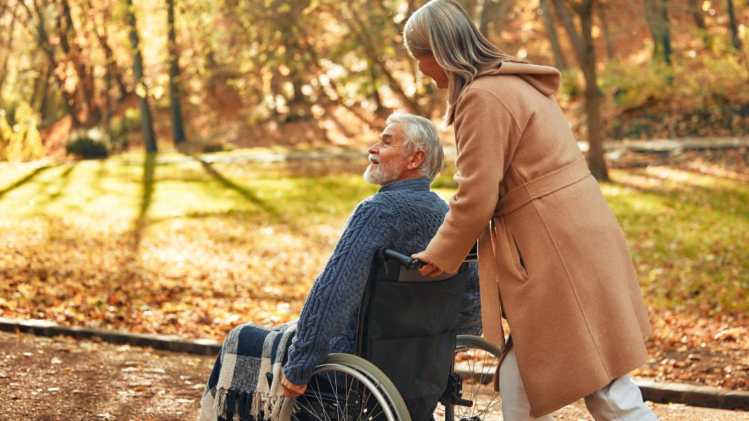 A Caregiver Joyfully Pushes A Senior In A Wheelchair