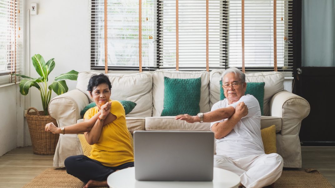 Exercising at home: Can digital technologies help? 1 Older adult couple sitting on their living room floor and stretching while look at an open laptop.