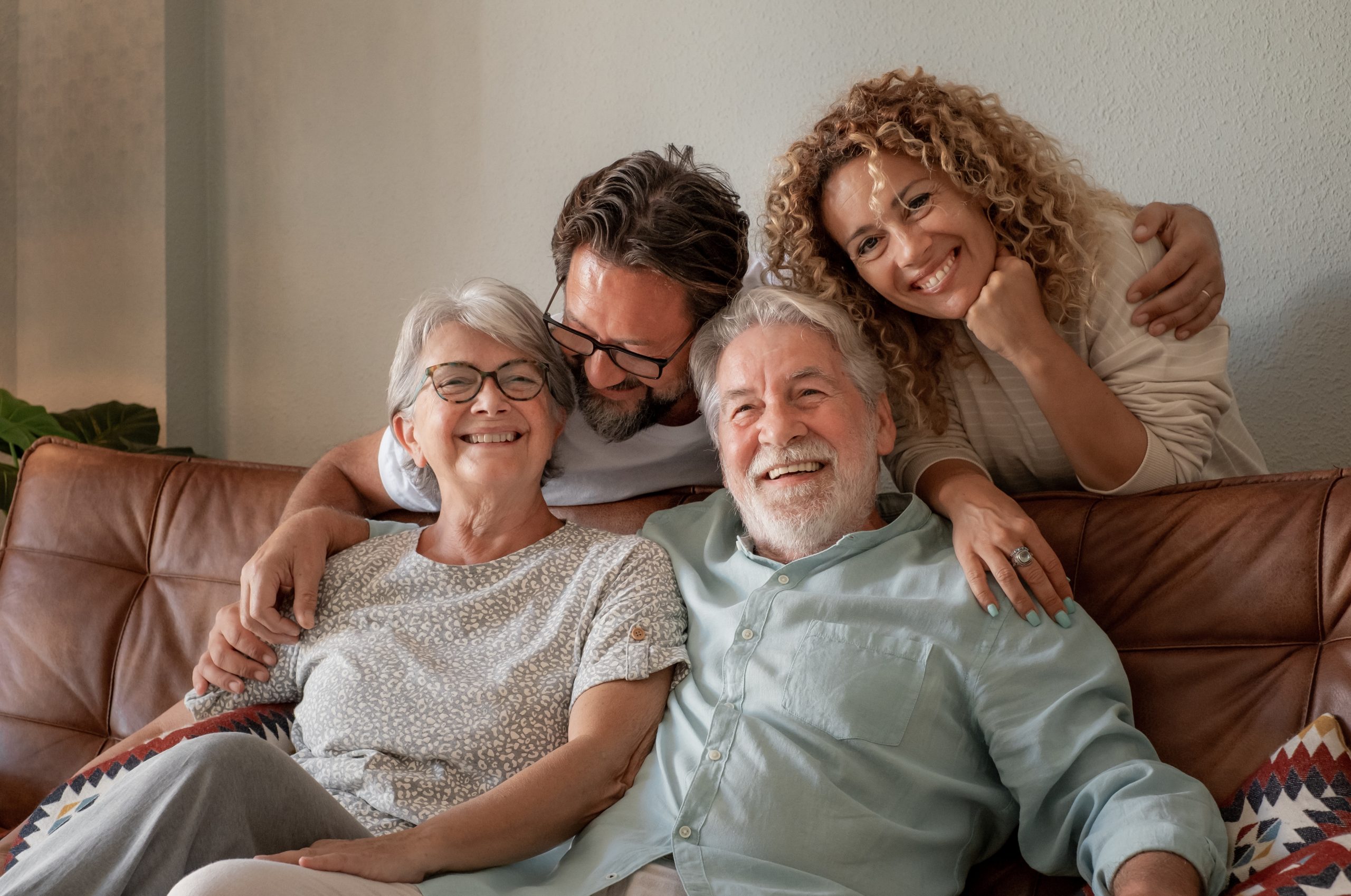 Newsletter Sign Up 1 An older couple sits on a couch, embraced by a younger couple behind them. All four are smiling.