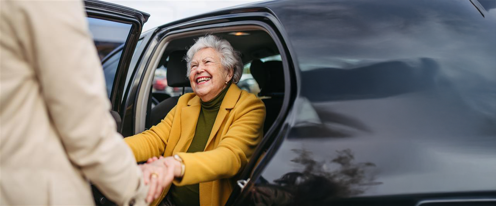 Inside a car, a woman and an older woman shake hands, conveying a warm and friendly interaction between them.