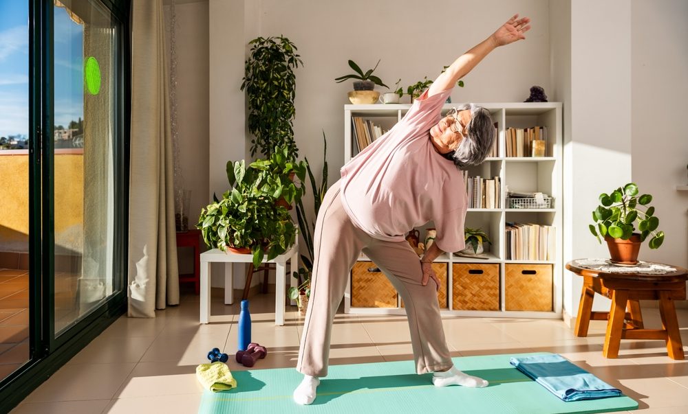 A Senior Woman Performs A Side Stretch At Home Standing