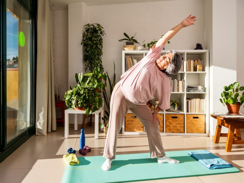 A Senior Woman Performs A Side Stretch At Home Standing