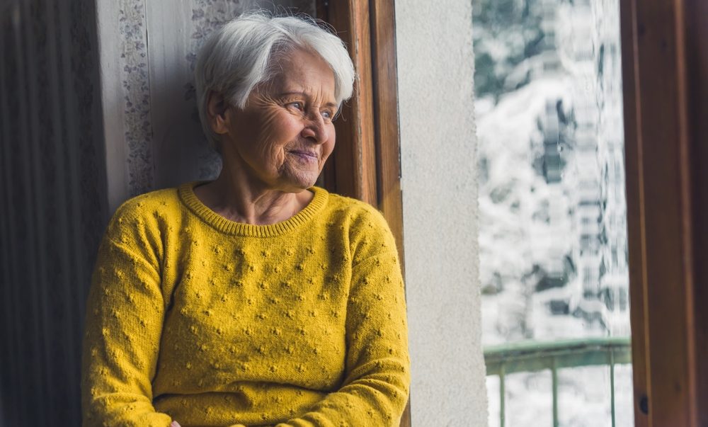 Senior in yellow sweater by window - Supporting a Loved One Through the Winter Blues
