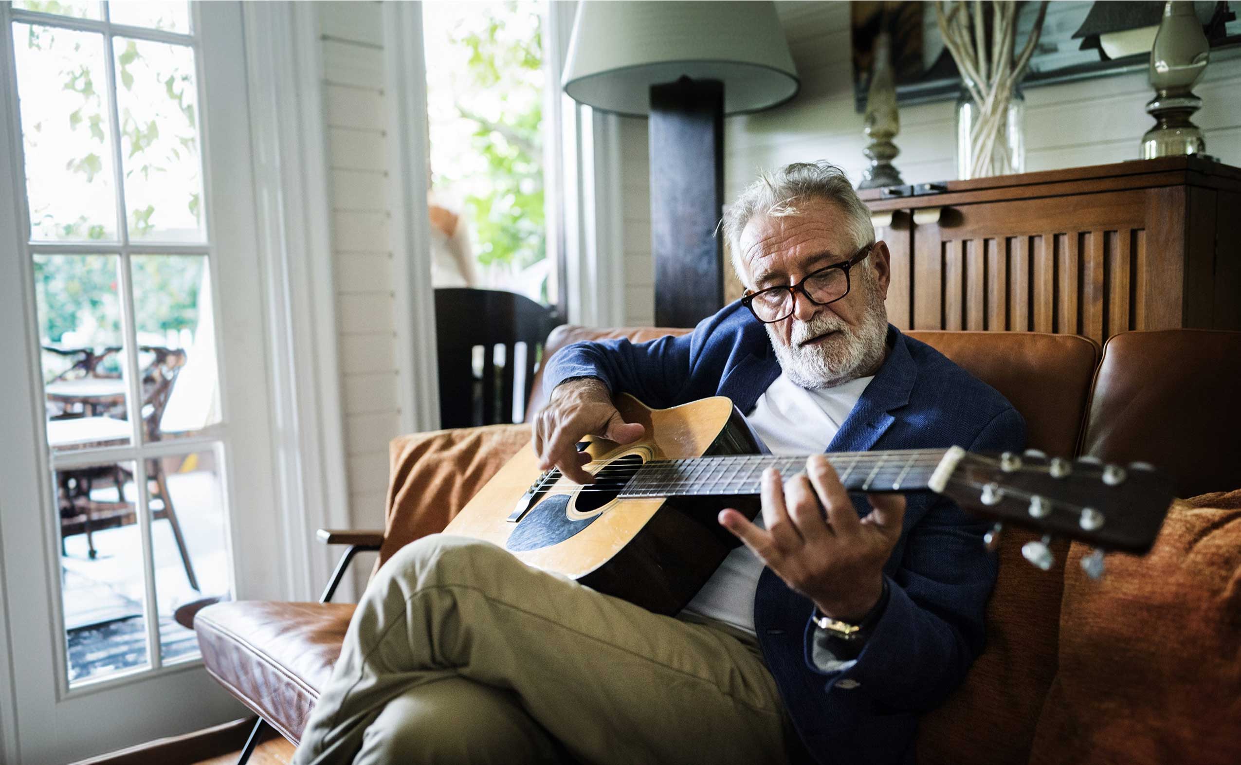Elderly man playing guitar indoors.