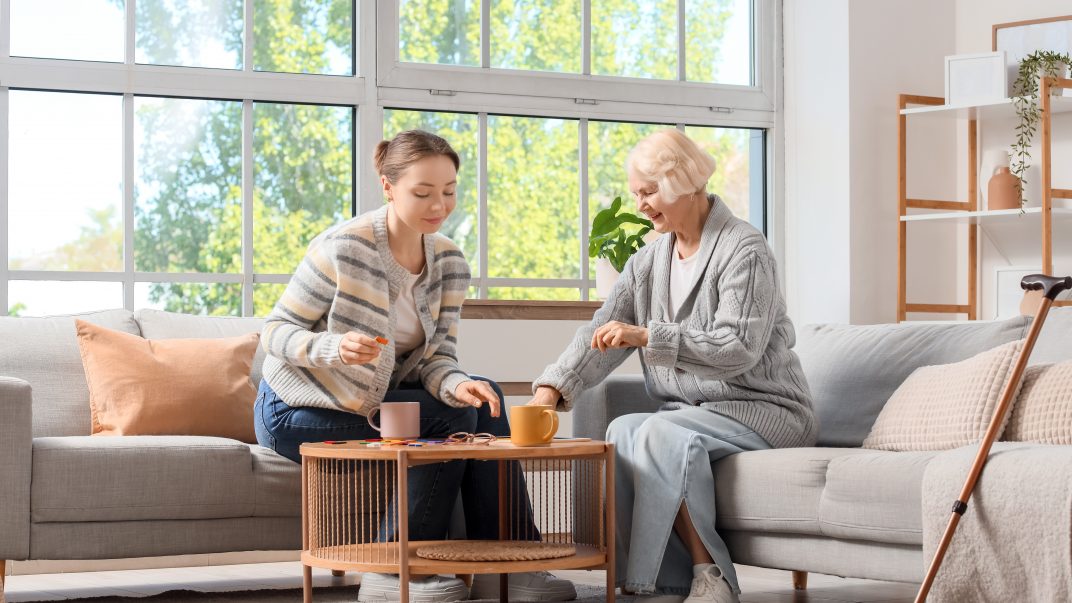 Understanding Alzheimer’s: How Families Can Support a Loved One at Home 1 Caregiver and elderly woman enjoying tea together indoors.