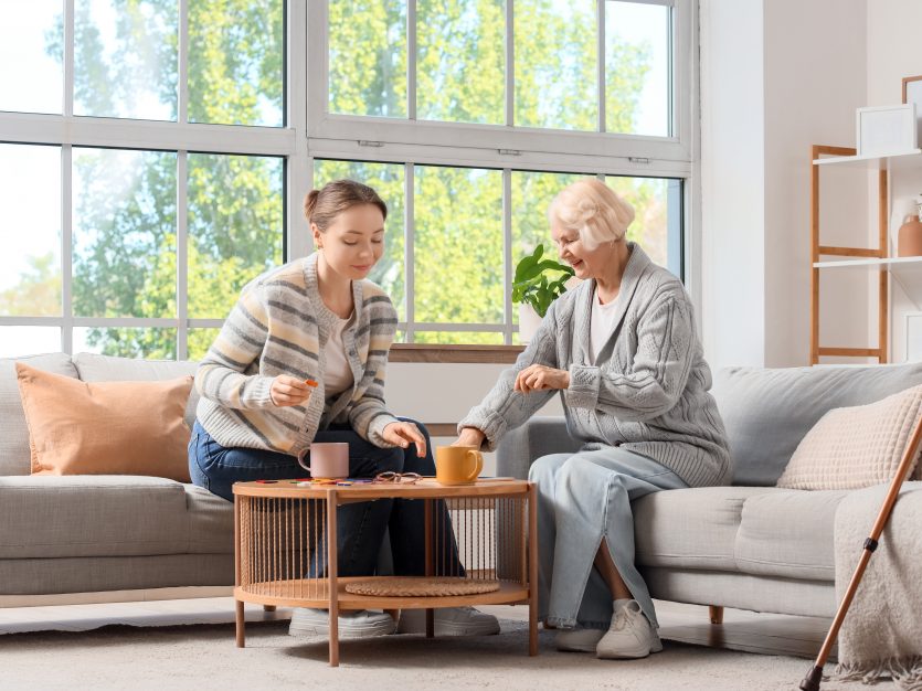 Caregiver and elderly woman enjoying tea together indoors.