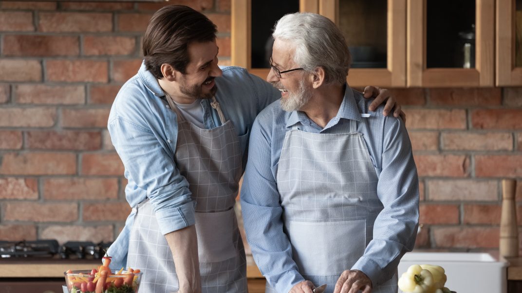 More than a card: What World Senior Citizens Day reminds us about connection 1 Elderly man and son cooking together, smiling.