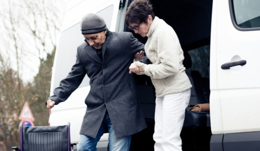 Woman assisting a man down steps of a van to a wheelchair