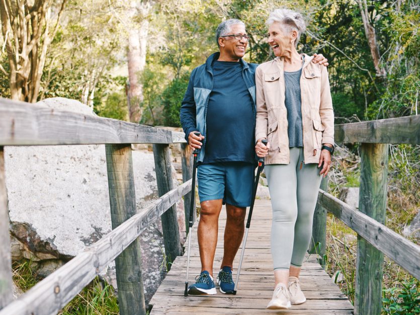 Older adult couple walking over a bridge with ski poles.